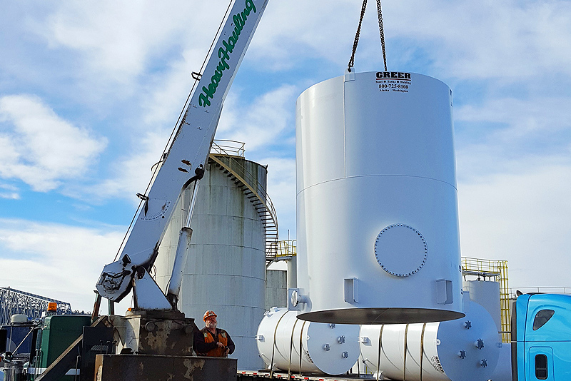A vertical stainless steel tank being lifted into place with a crane